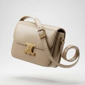 Bolso Celine modelo Triomphe en cuero liso beige con logo dorado. Incluye bandolera adaptable. Diseño elegante y atemporal.
